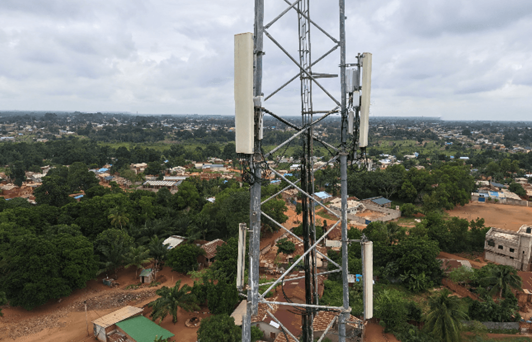 Vue aérienne du sommet d'un pylône télécom — antennes panneaux et installations urbaines en arrière-plan